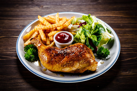 Roasted chicken leg with french fries and vegetable salad on wooden background