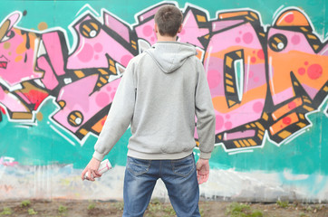 A young graffiti artist in a gray hoodie looks at the wall with