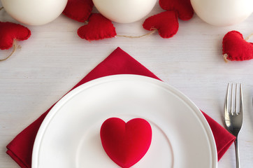 Beautiful table setting in white red tone for celebrate St Valentines Day. Decorative hearts and candles, plate and cutlery, red heart shape gift box. Love romantic dinner concept.