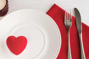 Beautiful table setting in white red tone for celebrate St Valentines Day. Plate, cutlery, line napkin and red heart shape gift box. Love romantic dinner concept.