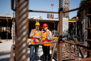 Architect  and structural engineer  in orange work vests and  helmets discuss a building project on the open air building site with a lot of steel frames