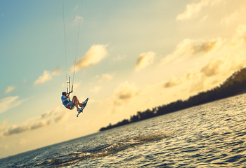 Fototapeta premium Young man kite boarder jumps over the sea at sunset 