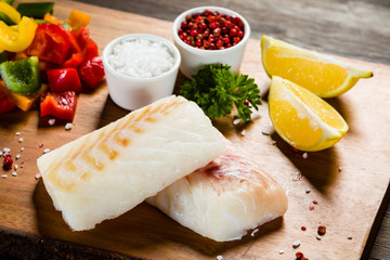 Fresh raw cod with herbs and vegetables served on cutting board on wooden table