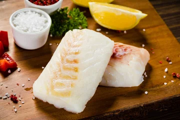 Rolgordijnen Vis Fresh raw cod with herbs and vegetables served on cutting board on wooden table