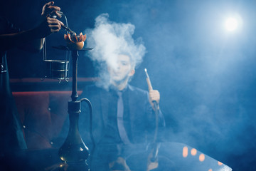 Smoking hookah, waiter changes coals and tobacco, in background is man shisha.