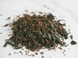 Trendy drink idea: Tea-Coffee Blend Combines Two Popular Drinks. Heap of dry mix of green tea and ground roasted coffee beans. Close up view. White marble tabletop.