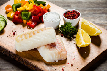 Fresh raw cod with herbs and vegetables served on cutting board on wooden table