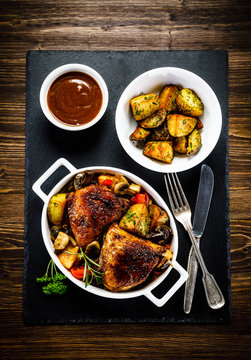 Grilled chicken legs with baked potatoes and vegetable salad on black stone plate