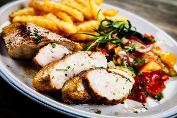 Grilled chicken fillet with french fries on wooden background
