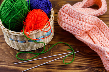 Wicker basket with colorful knitting yarns, knitting needles and knitted scarf on wooden table