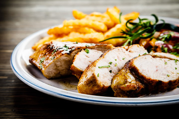 Grilled chicken fillet with french fries on wooden background