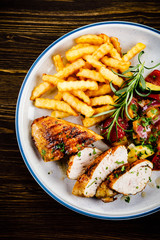 Grilled chicken fillet with french fries on wooden background
