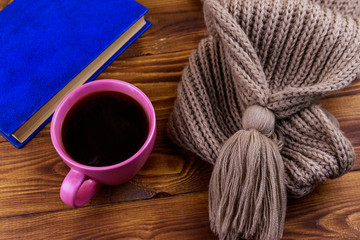 Cup of coffee, knitted scarf and book on wooden background