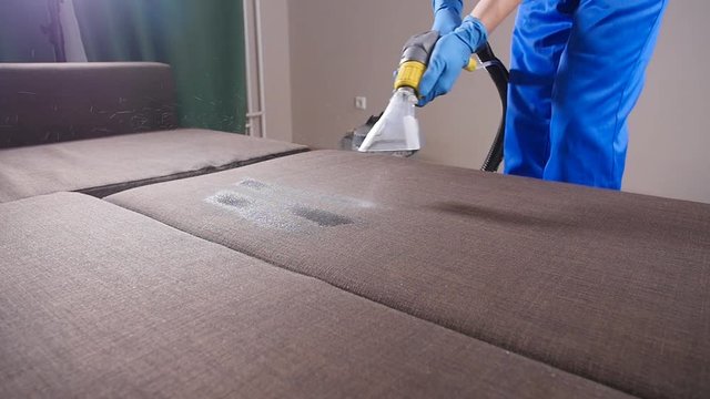 Concept of cleaning in the apartment and office. Dry cleaning worker removing dirt from sofa indoors