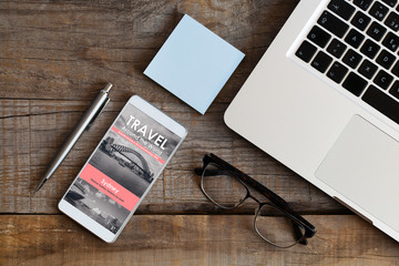 Top view of office desk and mobile phone with travel news website in the screen.