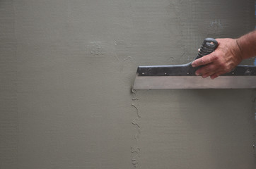 Hands of an old manual worker with wall plastering tools renovating house. Plasterer renovating...