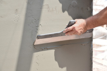 Hands of an old manual worker with wall plastering tools renovating house. Plasterer renovating...