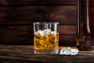 Golden bourbon whiskey with ice on a rustic wooden table in a distillery or bar