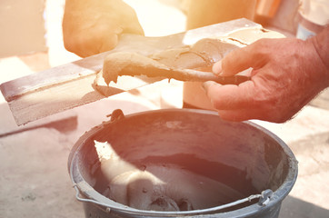 Hands of an old manual worker with wall plastering tools near the bucket with reinforcing mixture....