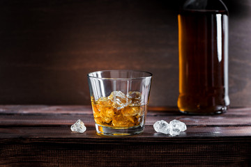 Golden bourbon whiskey with ice on a rustic wooden table in a distillery or bar