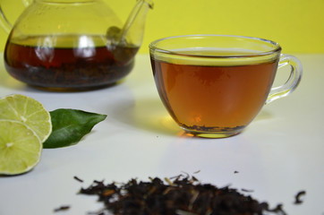 Transparent cup and teapot with black tea, dry tea brewing on the table, bergamot slices, or lemon or lime on a white background