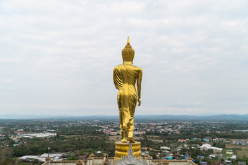 Standing buddha image, golden statue at Nan’s Khao Noi mountain temple, northern Thailand, looking deep and wide at the otherside of the city below.