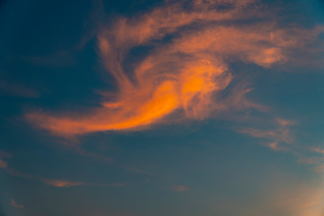 Blue sky with a reflection of the light of sunset at dusk on the cloudy shapes that look like an...