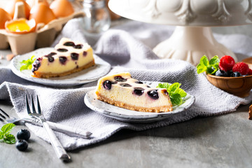 Blueberry cheesecake pieces, in selective focus, seem to be prepared for two persons on ceramic plates with mint leaf decoration for a delicious snack of the day.