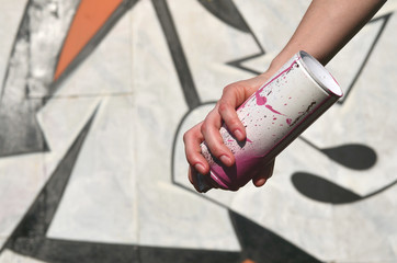 Photo of a girl's hand with aerosol paint cans in hands on a graffiti wall background. The concept...