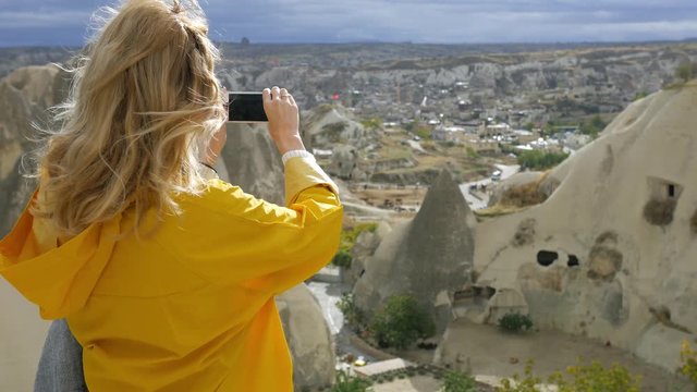 woman in a yellow raincoat shoots a rocky valley on phone