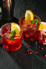 Delicious close up view on red alcoholic cocktail. Glass with ice, beverage, lemon and bar utensils on dark wooden background. Copy free space for your text, logo or brand.