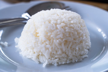 Steamed fragrance rice in a shape of an upside down bowl is served with a pair of fork and spoon on the table, background blurred.