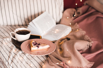 Cup of tea with cake and open book in bed close up. Good morning. Breakfast.