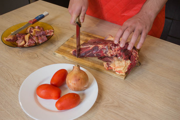 a man in a kitchen apron, meat on a board and a wooden table, a knife and vegetables