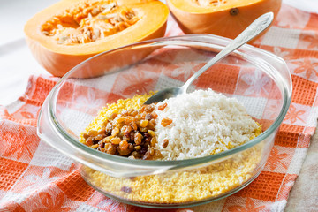 Raw washed millet, rice and raisins in a glass pan in the process of cooking milk pumpkin porridge