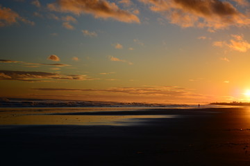 Fototapeta na wymiar Dramatic sunrise colours; beautiful sunrise on a beach and a lonely figure of a person walking along the beach.