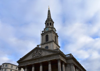 Fototapeta na wymiar St Martin in the Fields church from Trafalgar Square. Neoclassical facade and tower with spire, blue and golden clock. London, United Kingdom.