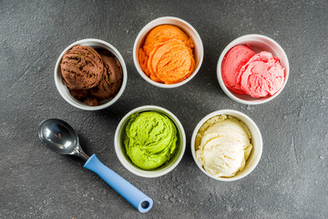 Colorful ice cream in little creamer bowls, sweet homemade summer dessert, black concrete background copy space top view