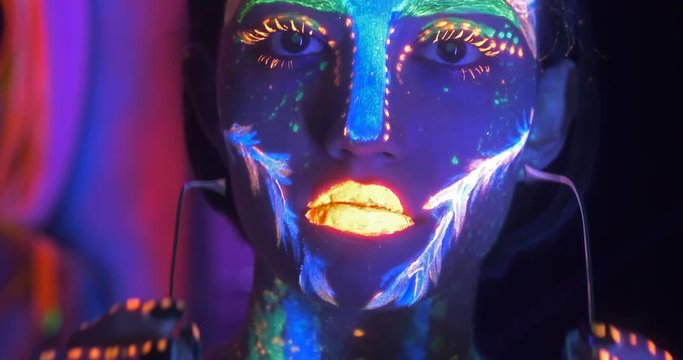Portrait of Beautiful Fashion Woman in Neon UF Light taking off fashion glasses. Model Girl with Fluorescent Creative Psychedelic MakeUp.