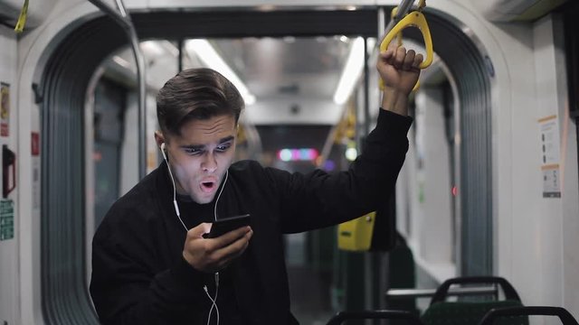 Happy businessman cheering celebrating looking at smartphone. Young urban professional successful business man receiving good news riding in public transport. He holds the handrail