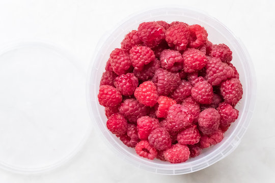 Ripe raspberries in a plastic bucket on a light background