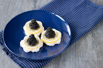 Canape with black caviar and a slice of lemon on a blue plate.