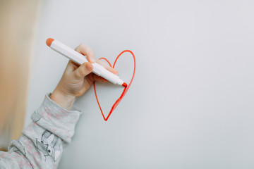 Girl draws heart with marker on a white blackboard. Mothers Day. Valentine's Day