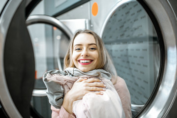 Portrait of a cheerful woman with clean and dried clothes in the laundry - obrazy, fototapety, plakaty