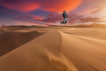 Fototapeta na wymiar Guy jumping in the desert on a sand dune at sunset.