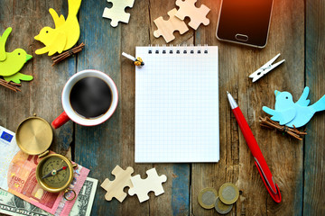 Rustic table with spiral notebook empty page, cup of hot coffee, smartphone, money, compass, pen...