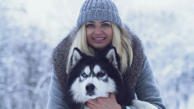 Portrait of pretty young woman holding and hugging fluffy siberian husky in the winter snow background. Dog on a winter walk in the forest.
