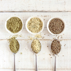 Organic hemp whole seeds, hulled seeds and protein powder in bowls and spoons on a white wooden background, closeup