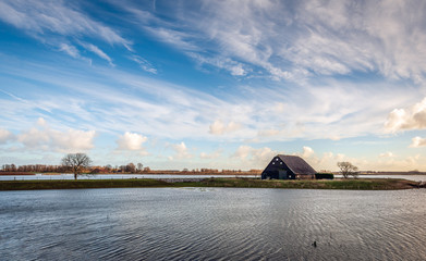 High water level in the Noordwaard polder of the Biesbosch, Noord-Brabant, the Netherlands. The old barn (built in 1900) is protected against the water by a ring dike. Its is a stormy day in winter. © Ruud Morijn