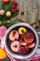 Hot mulled wine in a large pan on a wooden table. Fragrant traditional winter drink based on wine, juice, spices, seasonings, fruits. Top view.